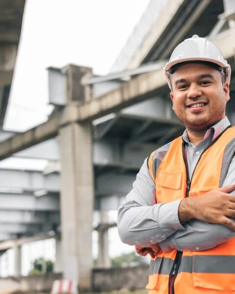 Indonesian engineer handsome man or architect standing confidently in front of a construction site with white safety helmet. Standing at highway concrete road site.