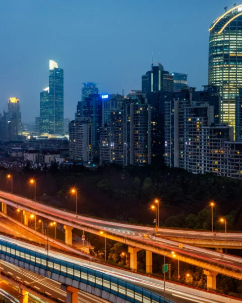 Night cityscape with illuminated buildings and busy multilevel highways showing light trails, showing the growth of Infrastructure Development Plans Indonesia.