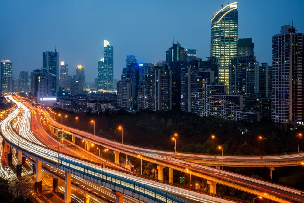 Night cityscape with illuminated buildings and busy multilevel highways showing light trails, showing the growth of Infrastructure Development Plans Indonesia.