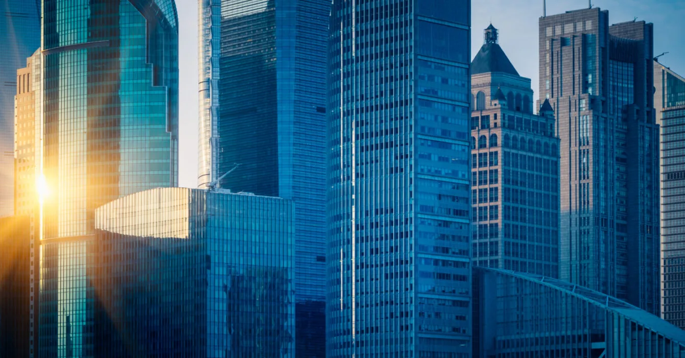 Sunrise peeking between modern skyscrapers in a dense urban cityscape to represent Public-Private Partnerships Indonesia.