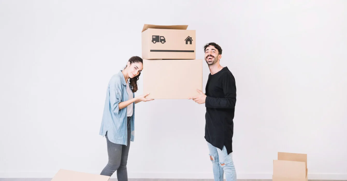 Indonesia Urbanization and Construction Growth represent by two people carrying cardboard boxes in a room with more boxes on the floor.