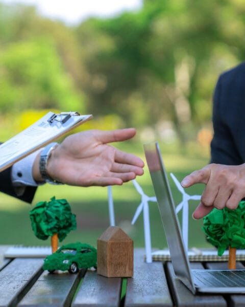 Professionals discussing over a laptop with model wind turbines and a green car on a table, showing Sustainable Infrastructure Projects Indonesia.