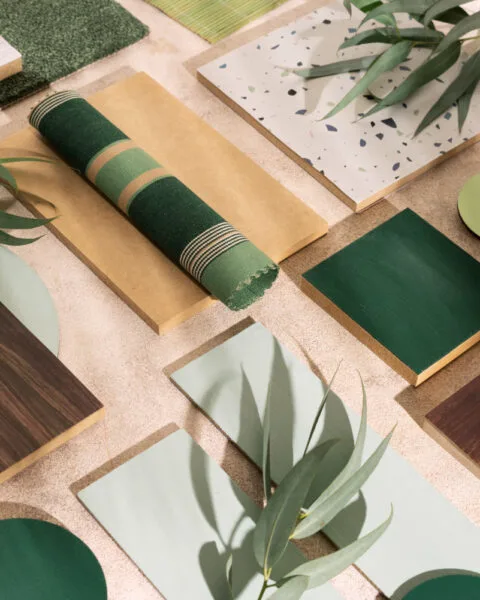 Indonesia Sustainable Materials Adoption: Flat lay of interior design materials in green and brown tones with fabric samples and leaves.